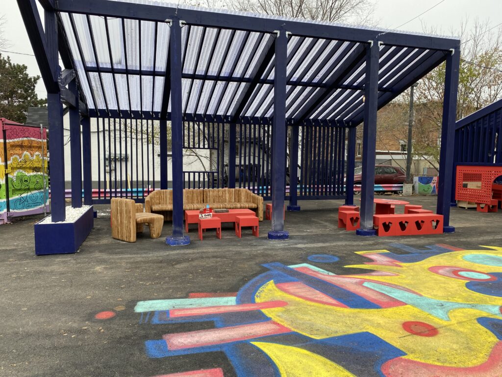 Outdoor seating area with wooden furniture, red tables, and colorful ground mural.