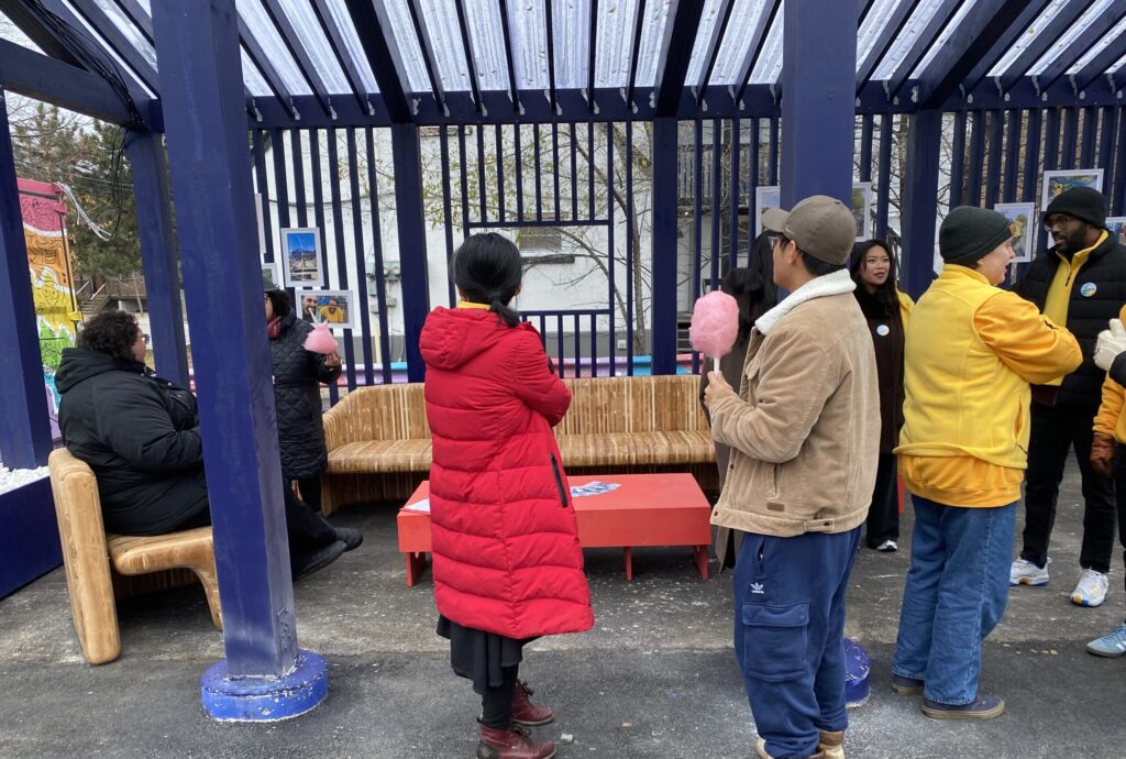People gathering and talking around the student-built seating under the blue-framed canopy.