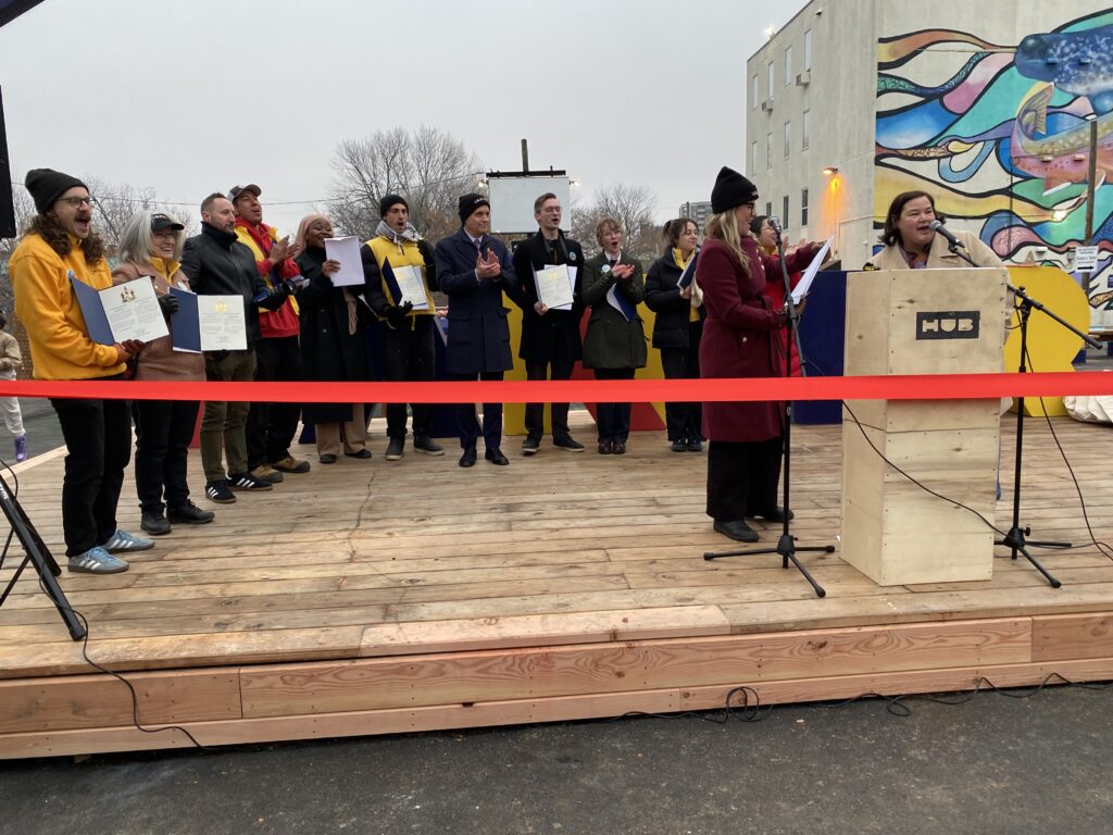 Group standing on the wooden stage holding certificates during the Vanier HUB opening ceremony.
