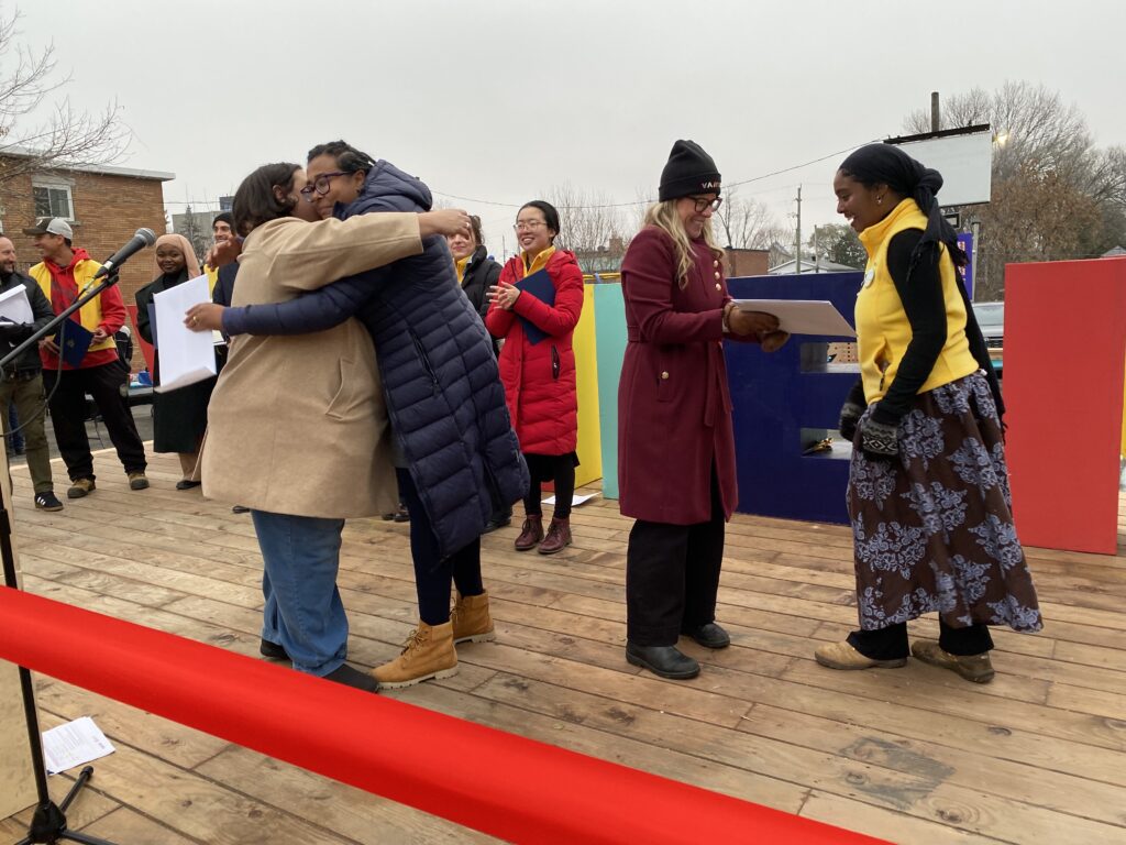 Participants exchanging documents and greeting each other on the HUB’s wooden stage during the opening event.