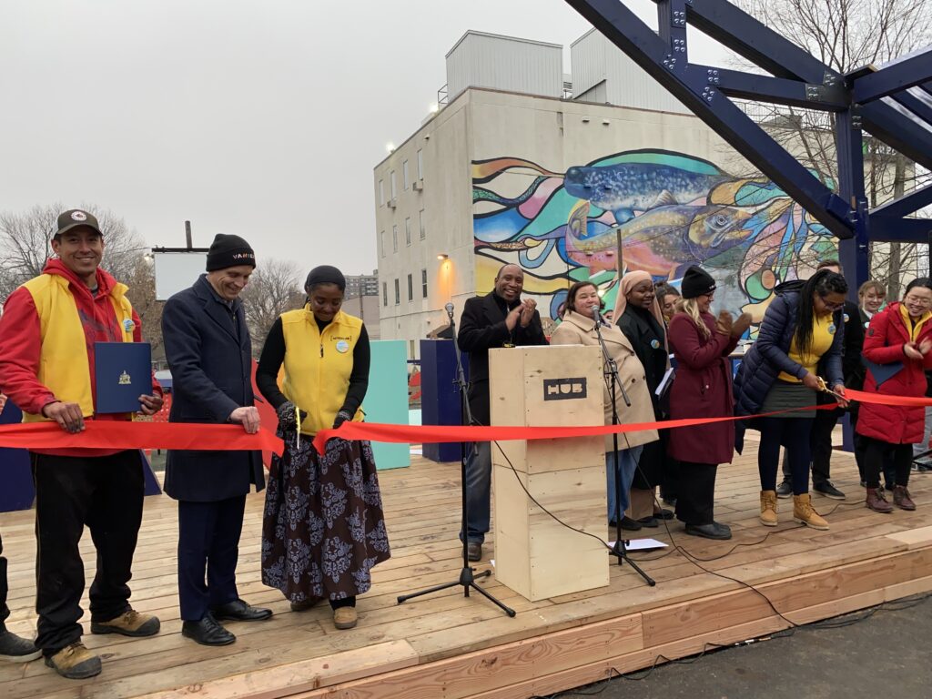 Ribbon-cutting moment on the HUB stage with participants gathered in front of the new blue-framed structure.