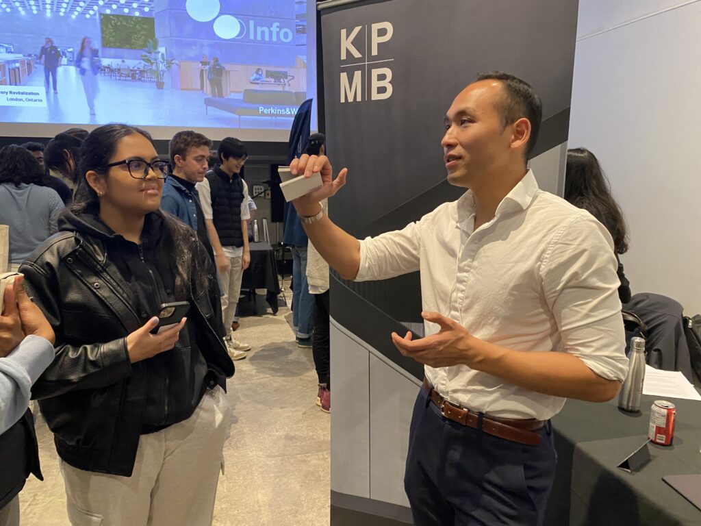 Ki Oh at KPMB booth gesturing while speaking to student
