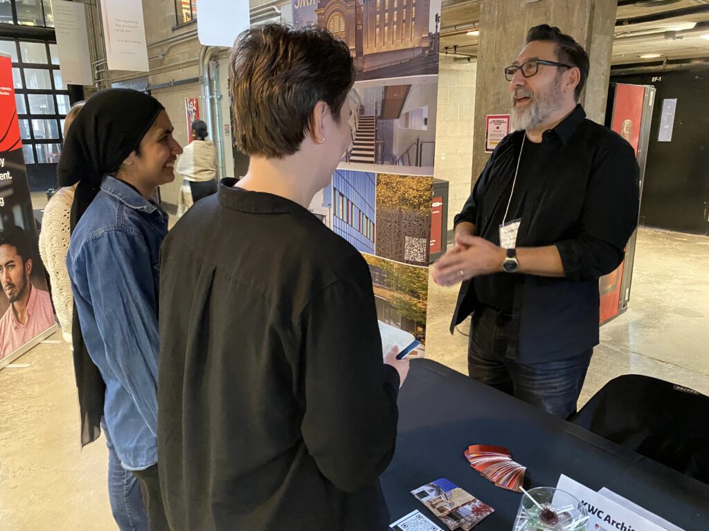 Laszlo Mohacsi speaking to three students at a table with a posters in the background.
