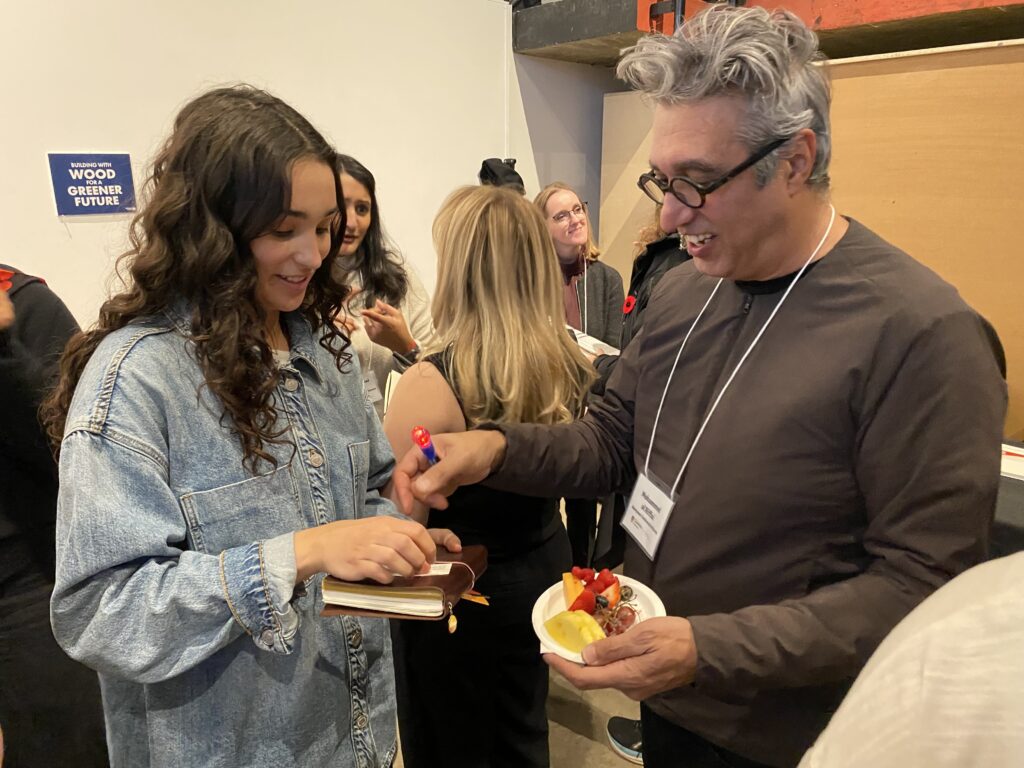 Mohammed al Riffai handing a business card to a smiling student holding a notebook.