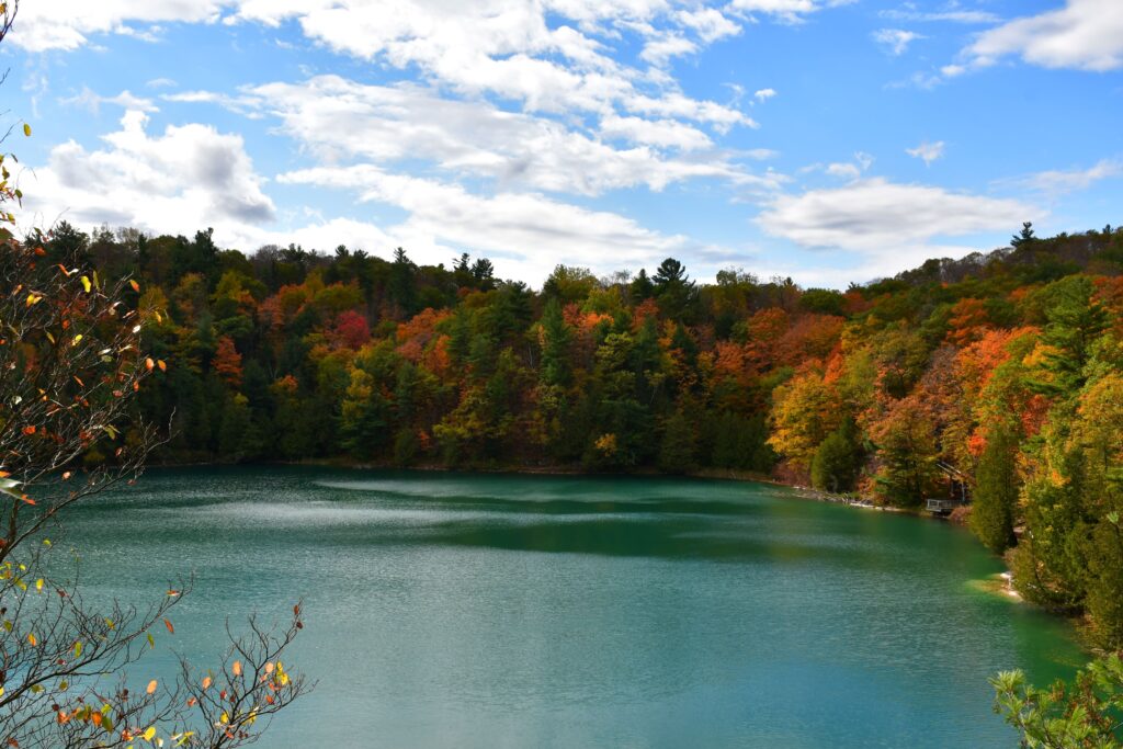 View of Pink Lake surrounded by colorful fall trees under a bright blue sky with.
