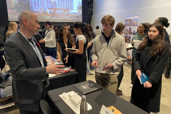Rick Kellner speaking to two students in front of a display table with a white architectural model.