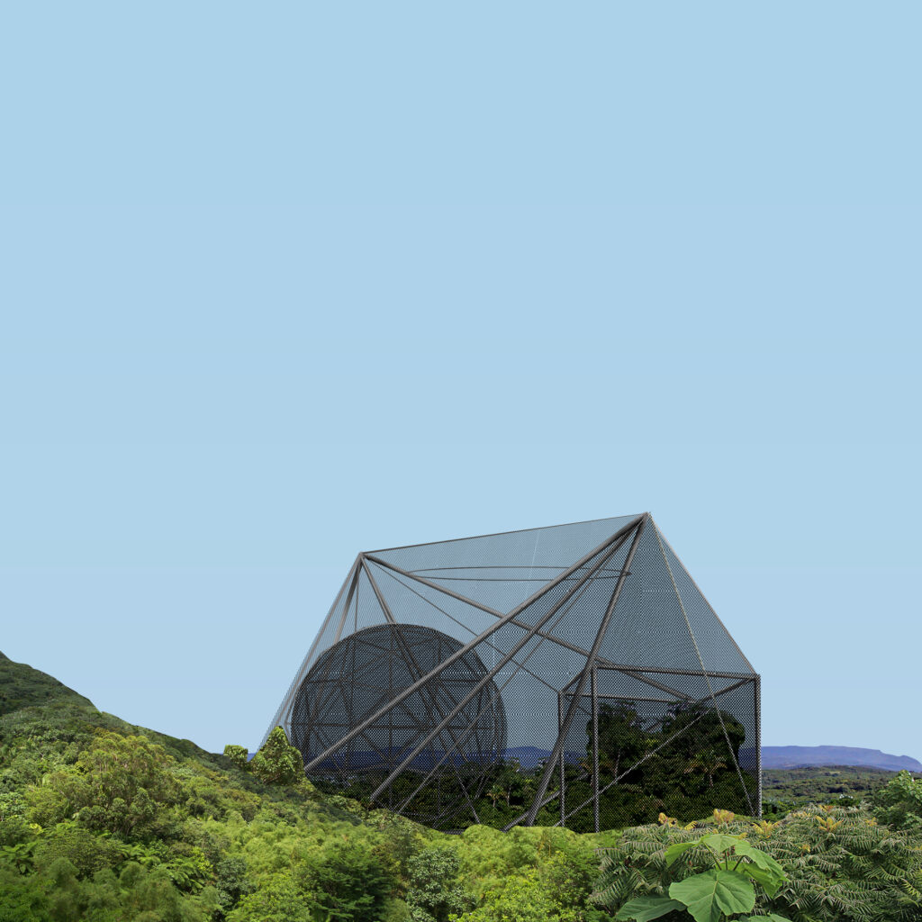 A geometric architectural structure with mesh walls enclosing tropical vegetation, set in a hilly forested landscape.