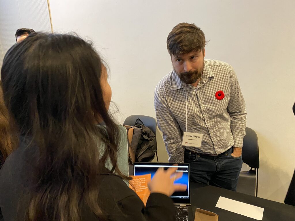 Stefan Gingras leaning forward listening to a student, with a laptop open on the table.
