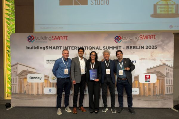 Five people stand on stage holding an award, in front of a backdrop reading “buildingSMART INTERNATIONAL SUMMIT – BERLIN 2025”.