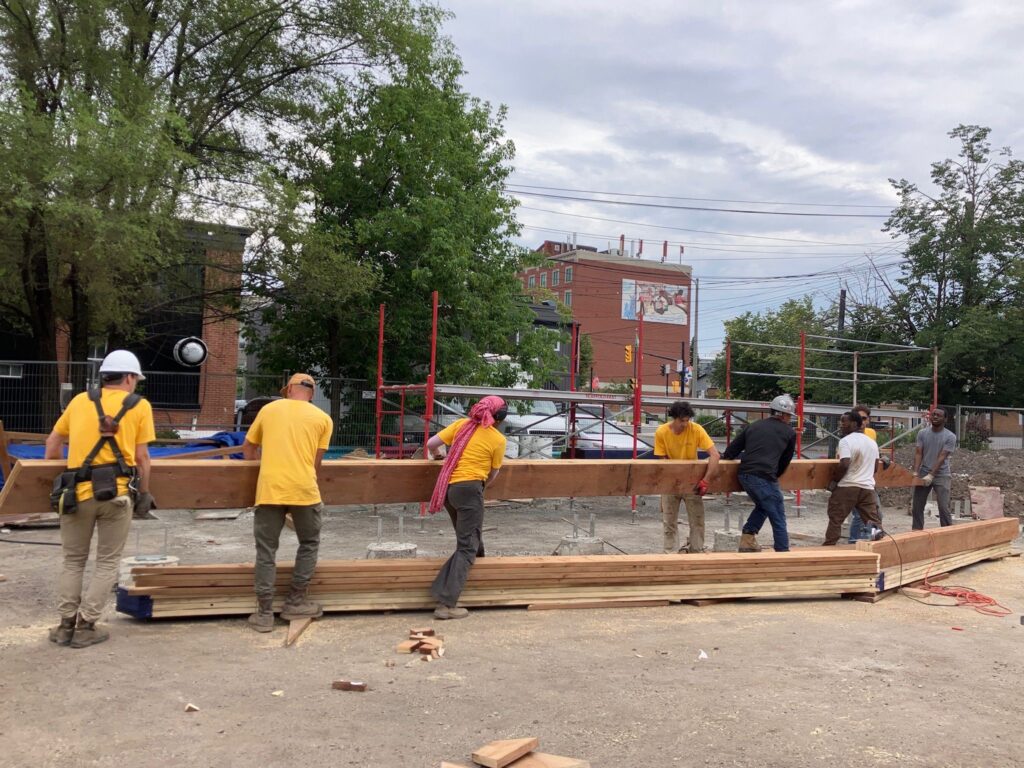 ASAU students lifting a long timber piece together during the construction of the blue-framed structures.