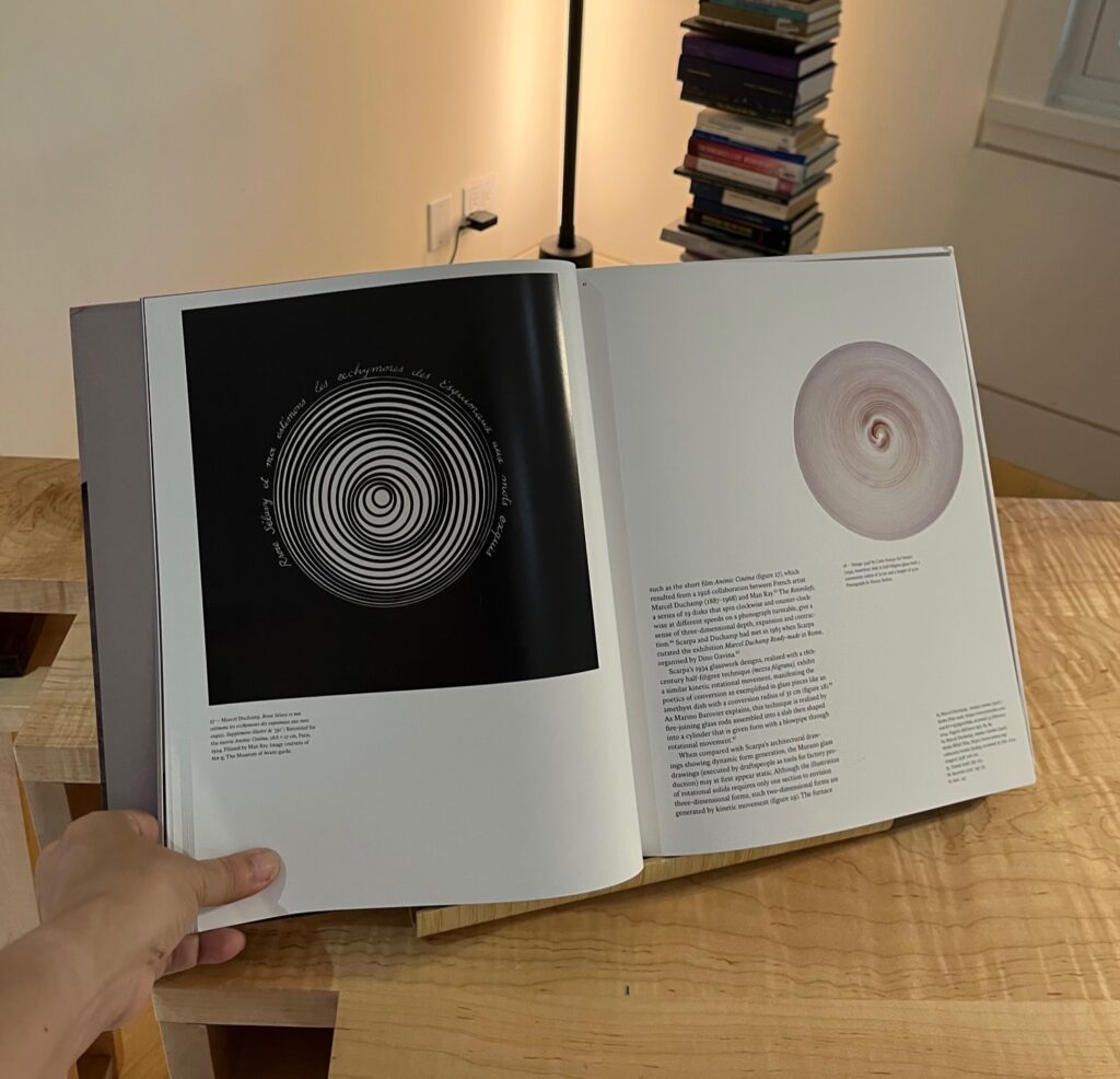 Person holding an open architecture book featuring images and text on Carlo Scarpa.