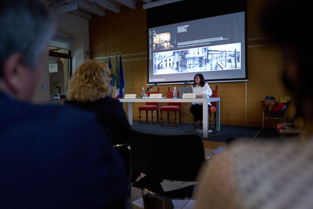 A speaker presenting architectural images on a screen to audiences in a lecture room.